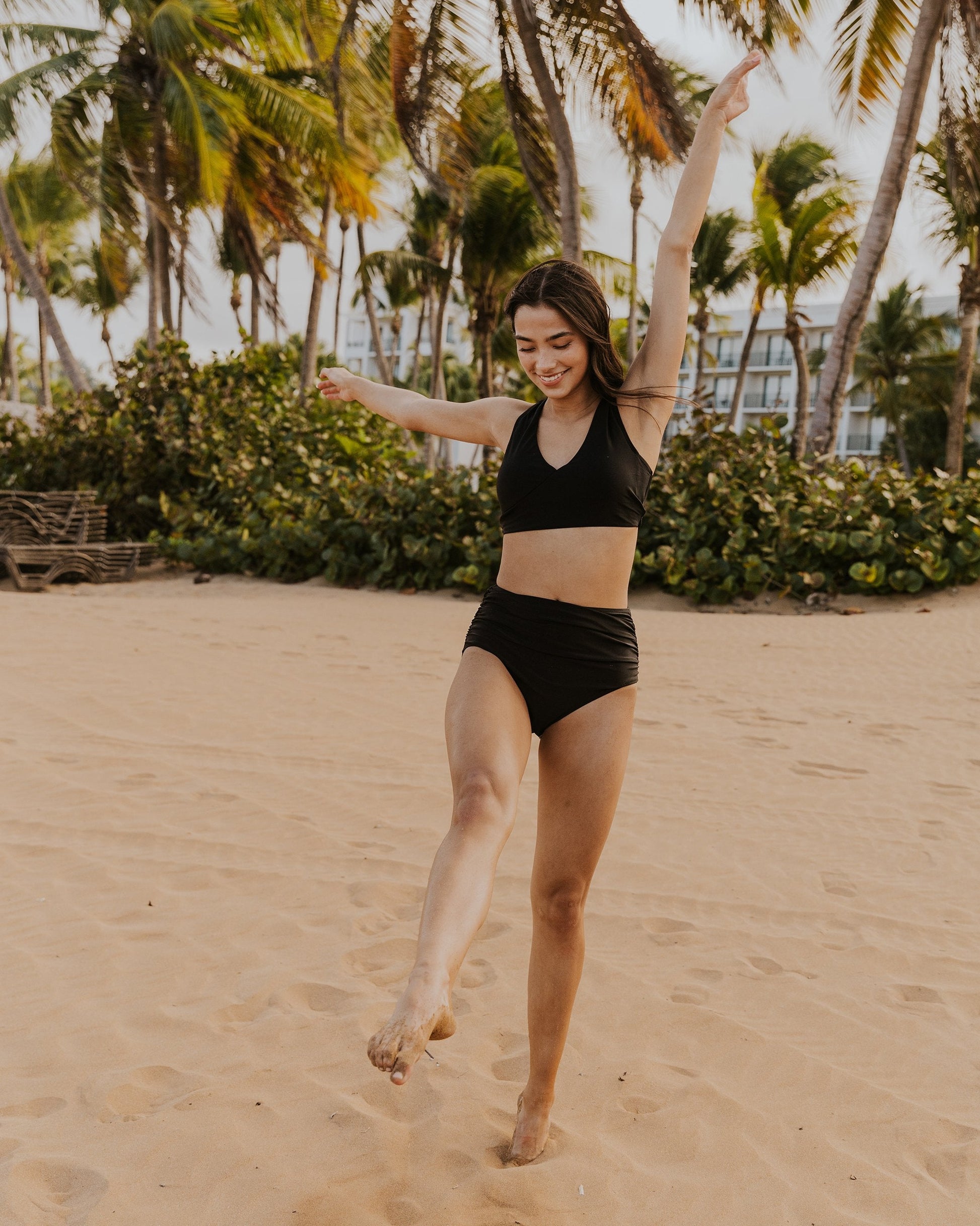 A women playing at the beach wearing black high waisted swim suit bottoms with a ruched detailing.